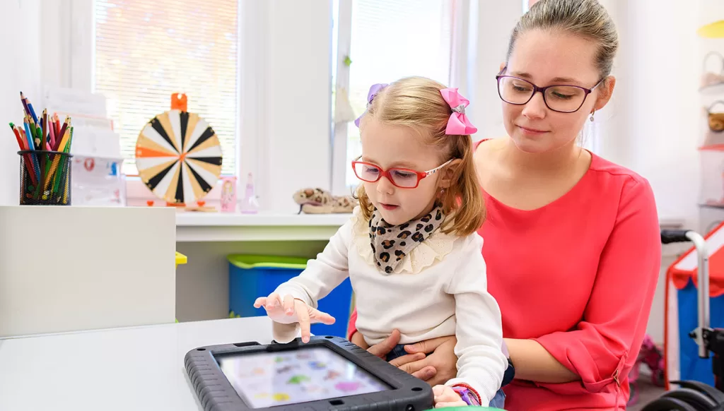 A woman holding a girl while she plays on a tablet computer